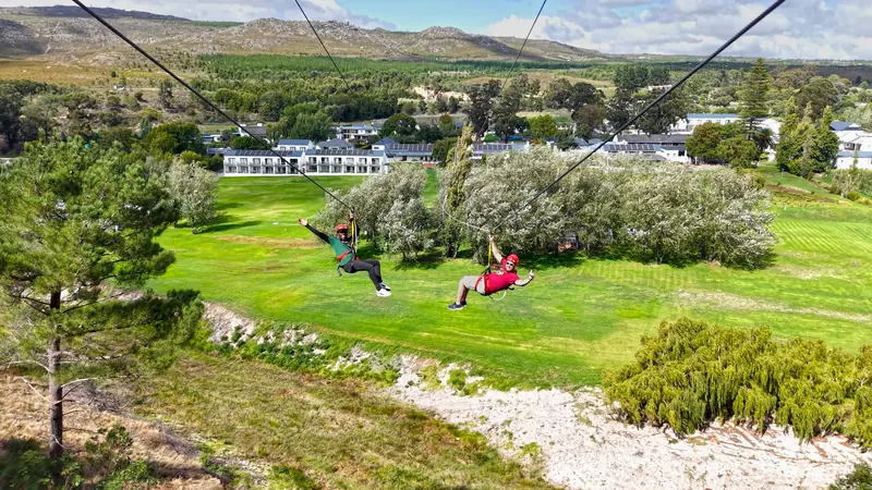 Aerial view of two riders on the Houw Hoek dual zipline above the hotel lawns