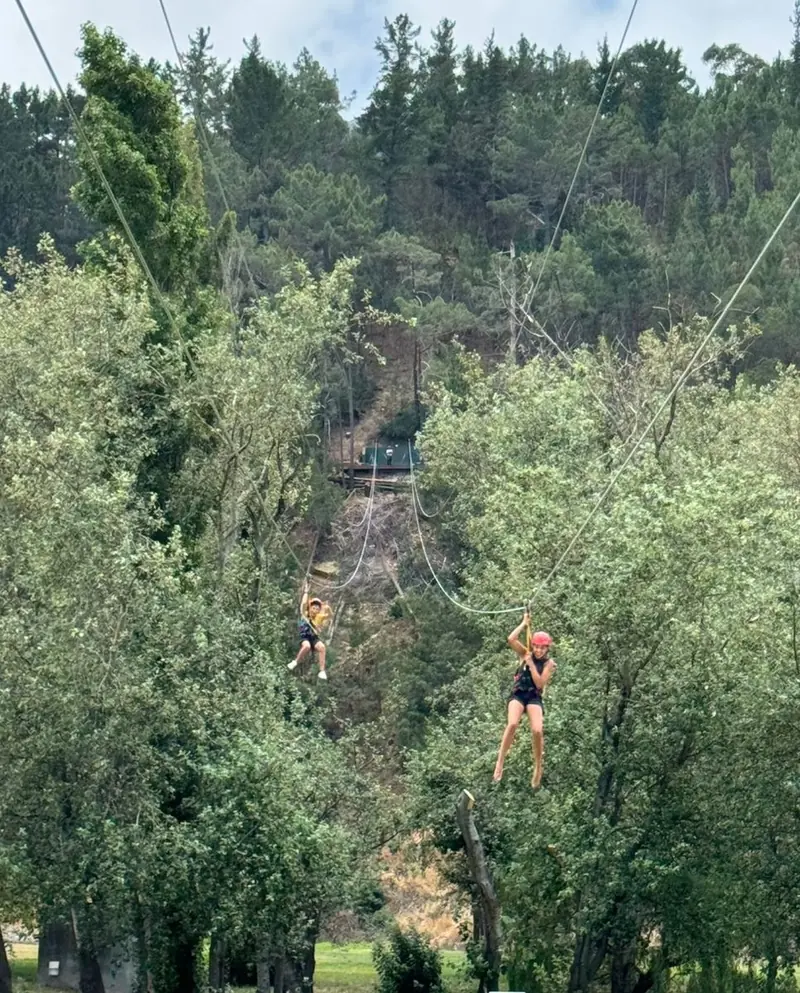 Two riders on the parallel cables at Houw Hoek Zipline, with the launch platform visible on the hillside behind them