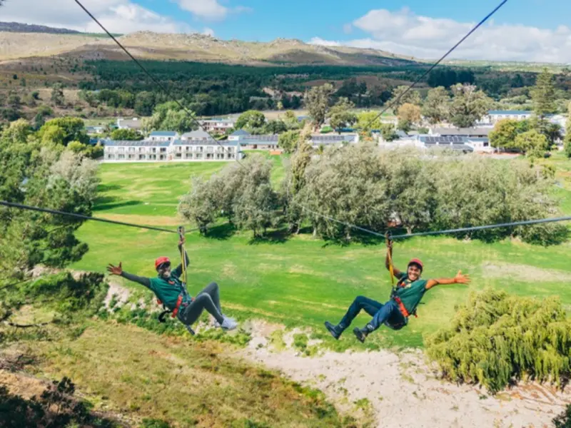 Two riders with arms outstretched sliding together down the Houw Hoek dual zipline